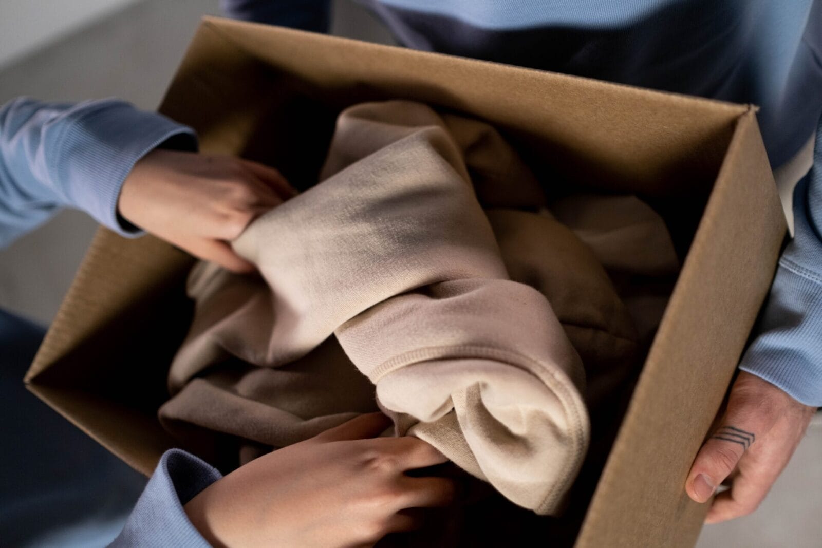 Hands dropping clothing into a cardboard box.